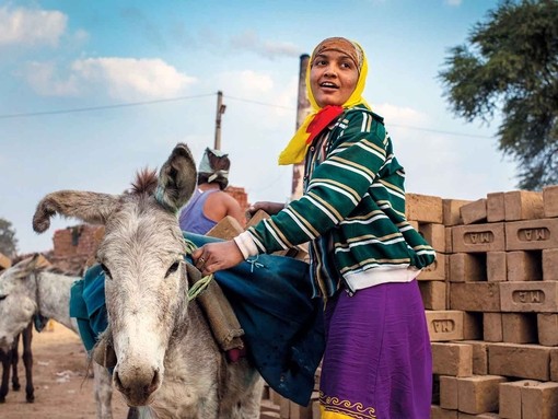 An image of a women wearing bright clothes holding a white donkey at a brick kiln site.