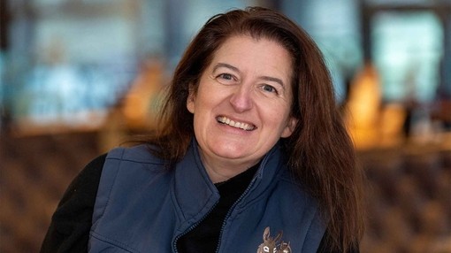 An image of a women with dark hair smiling toward camera while wearing a blue gilet with The Donkey Sanctuary logo.