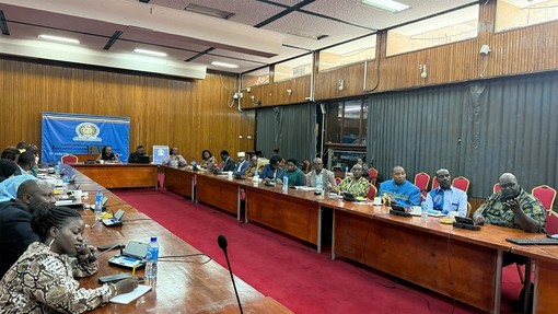 A conference room filled with people sitting at a long U shape desk