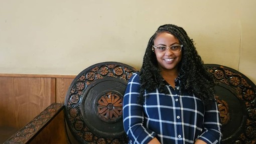 An image of a women wearing sunglasses sat on a carved wooden seat