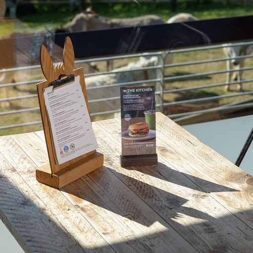 An image of a wooden table with with metal seats next to a large glass window which looks out over a field with donkeys.