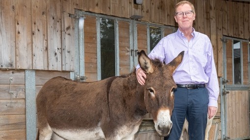 An image of a man stood next to a brown donkey looking toward camera.
