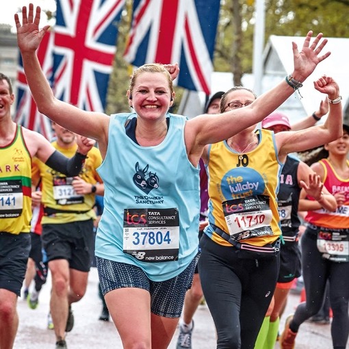 An image of a women running with her arms raised in celebration as she wears a blue vest with a logo featuring two donkeys.