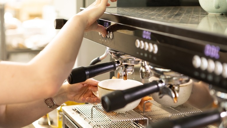 A close up image of a person pressing a button on a coffee machine while holding a coffee cup against the machine.