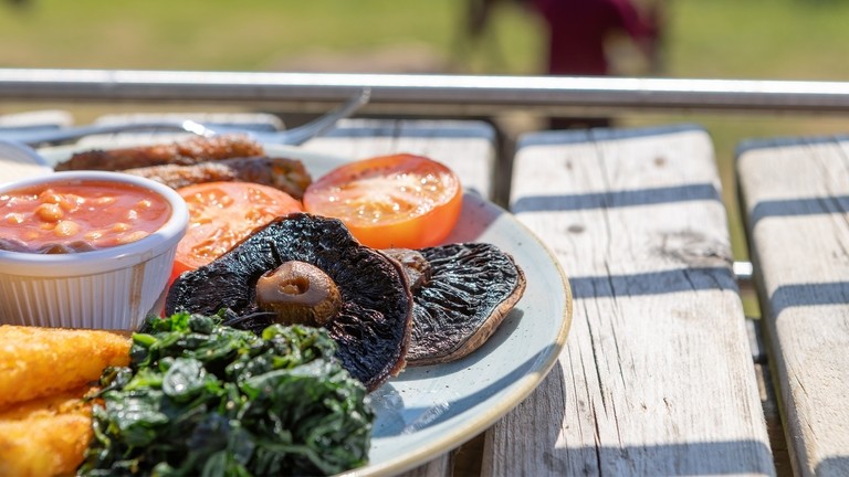A close up image of a vegetarian cooked breakfast on a wooden outdoor bench while a donkey grazes in the background.