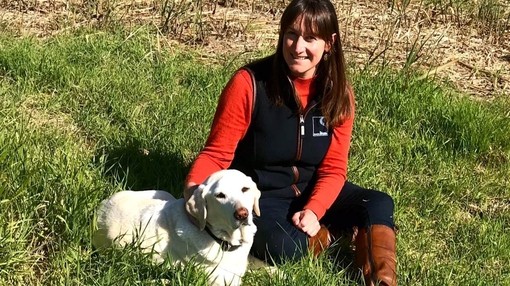 An image of a women sitting down next to a Labrador in a grass area. 