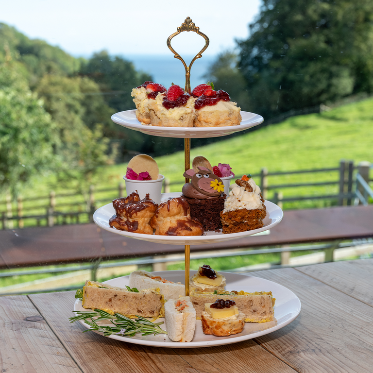 An image of a three tiered cake stand with sandwiches, cakes and scones placed on each tier. 